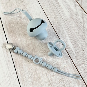 May include: A light blue silicone baby teether with a bone-shaped cutout, a light blue silicone pacifier, and a light blue silicone beaded pacifier clip with a bear-shaped charm.