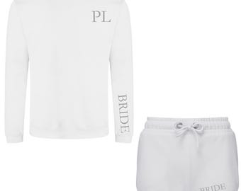 Puede incluir: Sudadera blanca de manga larga con la palabra "BRIDE" impresa verticalmente en la manga izquierda. La sudadera tiene "PL" impresa en la parte delantera. Pantalones cortos blancos con la palabra "BRIDE" impresa en la parte posterior.