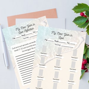 May include: A set of printable tarot card reflection sheets with the text "My Next Year in Love" and spaces to record the day, month, year, and tarot deck. Each sheet has spaces for 12 tarot cards. A white pen and a sprig of red berries are also visible.