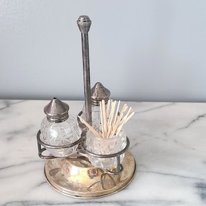 May include: A silver and glass salt and pepper shaker set with a toothpick holder. The set is on a gold metal stand.