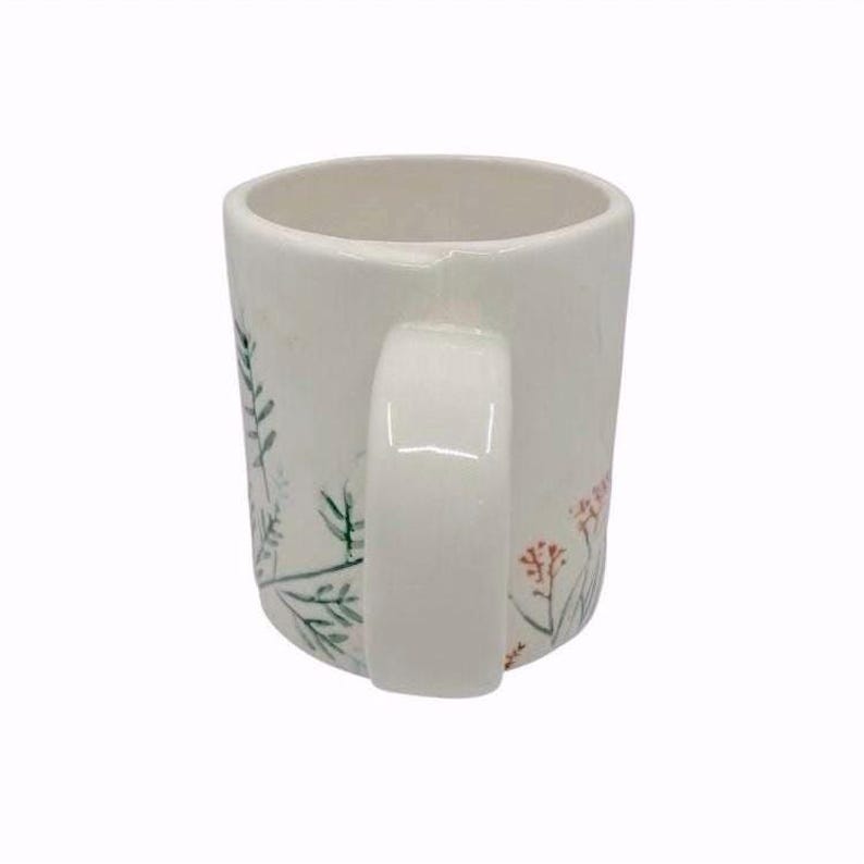 Pu&ograve; includere: Una tazza di ceramica bianca con un manico nero e la scritta "But First, Coffee" in grassetto nero. La tazza &egrave; appoggiata su una superficie di legno. La tazza &egrave; alta circa 10 cm.