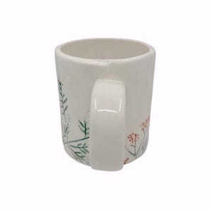 May include: A white ceramic mug with a curved handle. The mug is decorated with delicate floral and foliage designs in shades of green, red, and pink. The mug has a smooth, glossy finish.