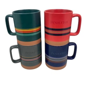 May include: Two tall ceramic mugs in shades of green, red, and blue, each with a large handle. The mugs feature horizontal stripes in various colours and the word "PENDLETON" embossed on the side. The mugs are stacked on top of each other.