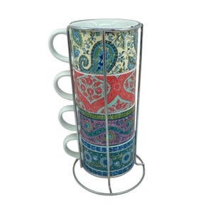 May include: A set of four stackable mugs with a colourful paisley pattern, held in a silver metal stand. Each mug has a white handle. The mugs are stacked vertically, with each level displaying a different design.