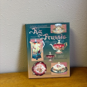 May include: A hardcover book titled Collector's Encyclopedia of R.S. Prussia Fourth Series by Mary Frank Gaston. The dark green cover features various color photographs of ornate porcelain teapots, bowls, and cups with floral patterns.