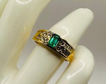 May include: A gold ring with a green emerald gemstone and small clear stones set in the band.