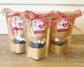 May include: Three brown paper bags filled with ingredients for hot chocolate. Each bag is tied with a red and white checkered ribbon and a gift tag that reads "Holiday Hot Cocoa" with a snowflake design. The tags also include the text "Merry Christmas!" and "From the Johnsons".
