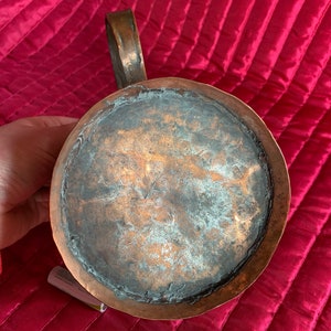 以下が含まれることがあります： 使い込まれた銅製のピッチャー。ピッチャーは、持ち手と丸い本体を持ち、底面が露出しており、銅本来の色合いが見て取れます。