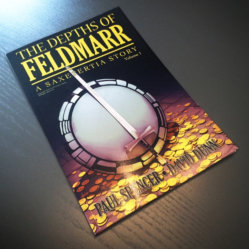May include: A book titled "The Depths of Feldmar: A Saxertia Story, Volume 1" by Paul Spencer and David Dunn. The cover features a circular design with a sword and gold coins.