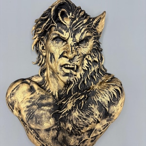 Könnte beinhalten: Eine Wandskulptur in Büstenform, die einen Menschen bei der Verwandlung in einen Werwolf darstellt. Die Figur hat ein gold-schwarzes Finish mit detaillierten Texturen, die auf einer Seite menschliche Züge und auf der anderen Fell zeigen, inklusive spitzer Zähne.
