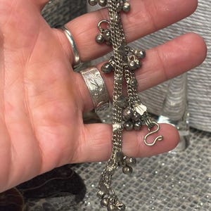 May include: Silver-toned anklet featuring multiple strands of delicate chains adorned with small, dangling bells. The anklet has a hook clasp for secure fastening. The design includes small heart-shaped charms.