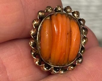 May include: A vintage gold-toned ring featuring an oval, orange coral stone with vertical ridges. The coral is set within a decorative, scalloped gold frame, showcasing a classic jewelry design.