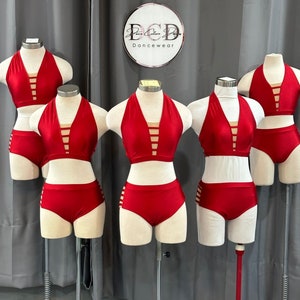 May include: Five red dancewear tops and bottoms on mannequins. The tops are halter style with a criss-cross design in the front. The bottoms are high-waisted with a side cut-out detail. The mannequins are on stands with wheels. The sign above the mannequins reads "ECD Dancewear".