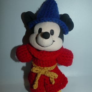 May include: A plush Mickey Mouse toy wearing a blue crocheted hat and a red crocheted robe with a gold belt.