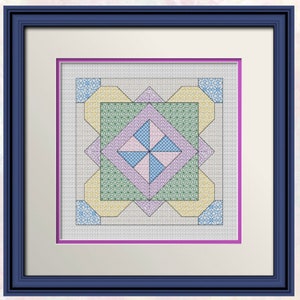Op de afbeelding: Een ingelijst kruissteekontwerp met een kleurrijk geometrisch patroon in tinten blauw, groen, geel en roze. Het ontwerp is gecentreerd in een witte passe-partout en een donkerblauwe lijst.