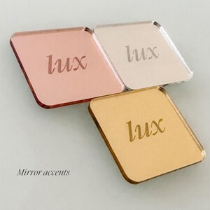 three square mirrors with the word "Lux" engraved on them, arranged in a triangular formation. Gold, Silver, Rose Gold