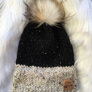 May include: Black and white knit beanie with a white pom pom and a brown leather patch that says "Lonis Knits".