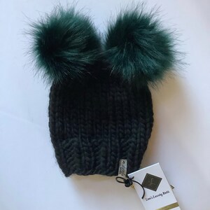 May include: Black knit beanie with two large green pom poms. The beanie has a tag that reads "Lori's Luxury Knits".
