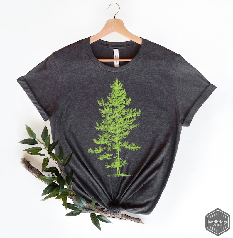 May include: A dark heather grey t-shirt with a green tree graphic. The t-shirt is on a hanger and has rolled up sleeves.