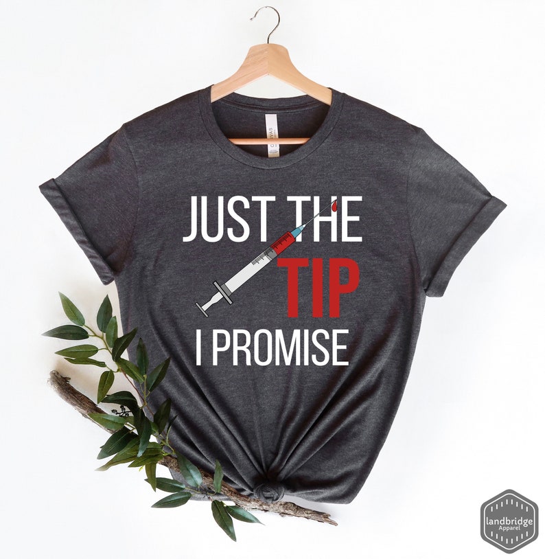 May include: Dark gray t-shirt with the text "Just the tip I promise" in white. A red and white syringe with a drop of red blood is above the word "tip".