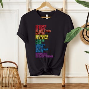 May include: Black t-shirt with a rainbow-colored graphic that reads "Science is real, Black Lives Matter, No Human is Illegal, Love is Love, Women's Rights are Human Rights, Kindness is Everything."