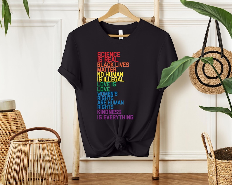May include: Black t-shirt with a rainbow-colored graphic that reads "Science is real, Black Lives Matter, No Human is Illegal, Love is Love, Women's Rights are Human Rights, Kindness is Everything."