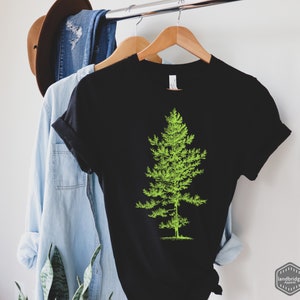 May include: Black t-shirt with a green silhouette of a pine tree on the front. The shirt is hanging on a hanger.