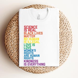 May include: White t-shirt with a rainbow-colored message that reads "Science is real, Black Lives Matter, No human is illegal, Love is love, Women's rights are human rights, Kindness is everything."