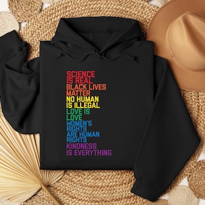 May include: Black hoodie with a rainbow-colored text print that reads "Science is real, Black Lives Matter, No Human is Illegal, Love is Love, Women's Rights are Human Rights, Kindness is Everything".