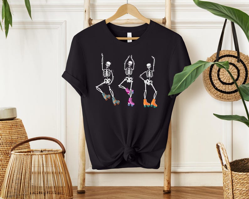 K&ouml;nnte beinhalten: Schwarzes T-Shirt mit einem Motiv von drei Skeletten, die Rollschuh laufen. Die Skelette tragen bunte Rollschuhe und sind in verschiedenen Posen.