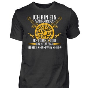 Könnte beinhalten: Ein dunkelgraues T-Shirt mit einem gelben Grafikdesign. Die Grafik zeigt einen Schild mit einem Knotendesign, zwei Schwertern und dem Text "ICH BIN EIN MANN DES NORDENS ICH FÜRCHTE ODIN UND MEINE FRAU DU BIST KEINER VON BEIDEN".