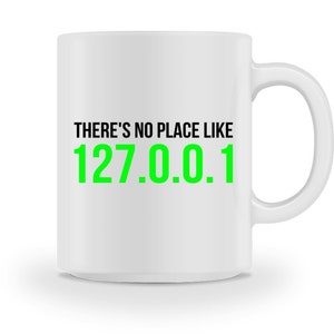 Könnte beinhalten: Eine weiße Keramik-Kaffeetasse mit schwarzem Text, der "There's no place like 127.0.0.1" lautet, wobei die Zahl grün ist.