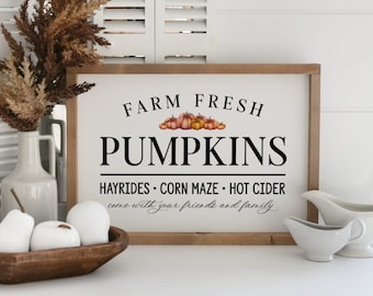 May include: A wooden sign with the text "FARM FRESH PUMPKINS" in black lettering. The sign also includes the text "HAYRIDES CORN MAZE HOT CIDER come with your friends and family." in smaller black lettering. There are five small orange pumpkins with green stems painted on the sign.