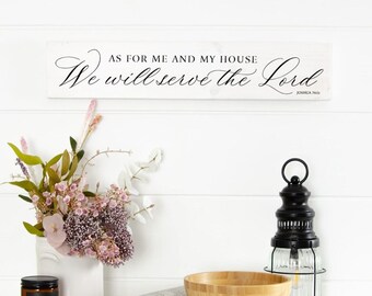 May include: A white wooden sign with the text "AS FOR ME AND MY HOUSE We will serve the Lord" in black script. The image also features a white vase with flowers, a black lantern, a wooden bowl, and a candle.