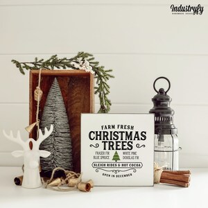 May include: White wooden sign with black text that reads "Farm Fresh Christmas Trees" with a green Christmas tree graphic. The sign also includes the text "Fraser Fir, Blue Spruce, White Pine, Douglas Fir, Sleigh Rides & Hot Cocoa, Open in December".