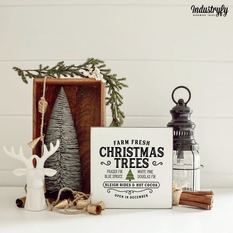 May include: White wooden sign with black text that reads "Farm Fresh Christmas Trees" with a green Christmas tree graphic. The sign also includes the text "Fraser Fir, Blue Spruce, White Pine, Douglas Fir, Sleigh Rides & Hot Cocoa, Open in December".