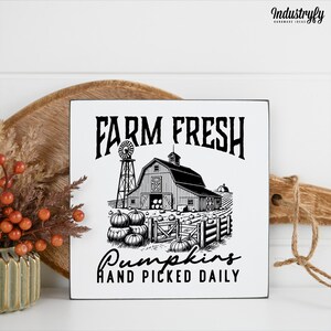 Könnte beinhalten: Quadratisches, weißes Holzschild mit schwarzem Text und einer Illustration einer Farm. Der Text lautet "FARM FRESH" über einer Illustration einer Scheune, Windmühle und Kürbissen. Darunter steht "Pumpkins HAND PICKED DAILY".