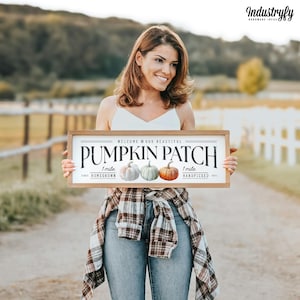 Könnte beinhalten: Ein Holzschild mit dem Text "Willkommen auf unserem wunderschönen Kürbisfeld" und drei Illustrationen von Kürbissen. Das Schild zeigt auch "1 Meile heimisch angebaut" und "1 Meile handverlesen".