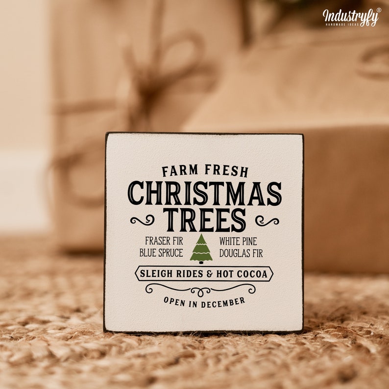 May include: White wooden sign with black text that reads "Farm Fresh Christmas Trees" with a green Christmas tree icon. The sign also lists types of trees, "Fraser Fir, Blue Spruce, White Pine, Douglas Fir" and says "Sleigh Rides & Hot Cocoa, Open in December."