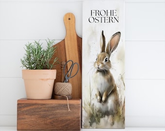 May include: A white canvas print with a watercolor painting of a brown rabbit standing in a field of green grass. The text "Frohe Ostern" is printed in black at the top of the canvas.