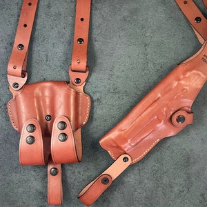 May include: A brown leather shoulder holster with two straps and a magazine pouch. The holster has a snap closure and is labeled "Safariland P2331".
