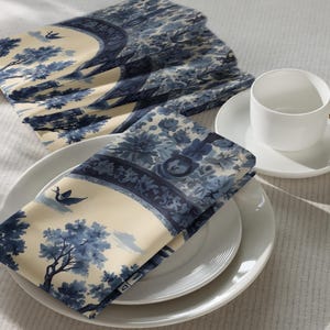 May include: Blue and white patterned fabric napkins folded on a white plate. The pattern features a blue and white floral design with a bird.