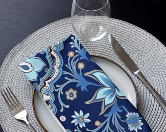 May include: A blue and white patterned cloth napkin with a floral design. The napkin is folded and placed on a white plate with a silver knife and fork on a gray placemat.