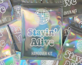 May include: A pile of iridescent silver pouches with a white disco ball graphic and the text "Stayin' Alive" and "Hangover Kit".