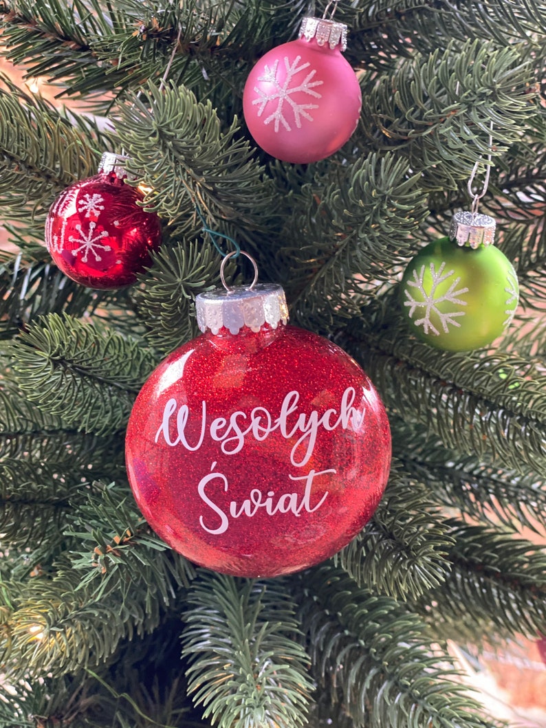 K&ouml;nnte beinhalten: Ein roter Weihnachtsbaumschmuck mit Glitzer und dem Text "Wesołych Świąt" in wei&szlig;en Buchstaben.