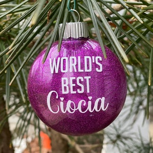 Könnte beinhalten: Lilafarbener Glitzer-Weihnachtsbaumschmuck mit dem Text "WORLD'S BEST Ciocia" in weißen Buchstaben.
