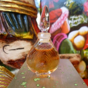 Könnte beinhalten: Eine durchsichtige Glasflasche mit einer goldfarbenen Flüssigkeit. Die Flasche hat eine strukturierte Oberfläche und eine runde, bauchige Form. Die Flasche steht auf einer Holzoberfläche.