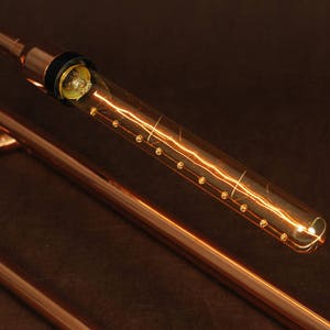 May include: A copper pipe lamp with a clear glass bulb that has a filament that looks like lightning. The bulb is lit and the light is casting a warm glow.