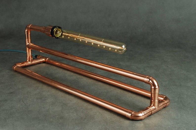May include: A copper pipe table lamp with a clear glass bulb. The lamp has a simple, industrial design.