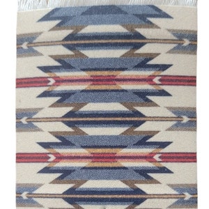 May include: A square coaster with a fringed edge features a geometric pattern in shades of blue, brown, red, and white. The pattern is reminiscent of Native American designs.